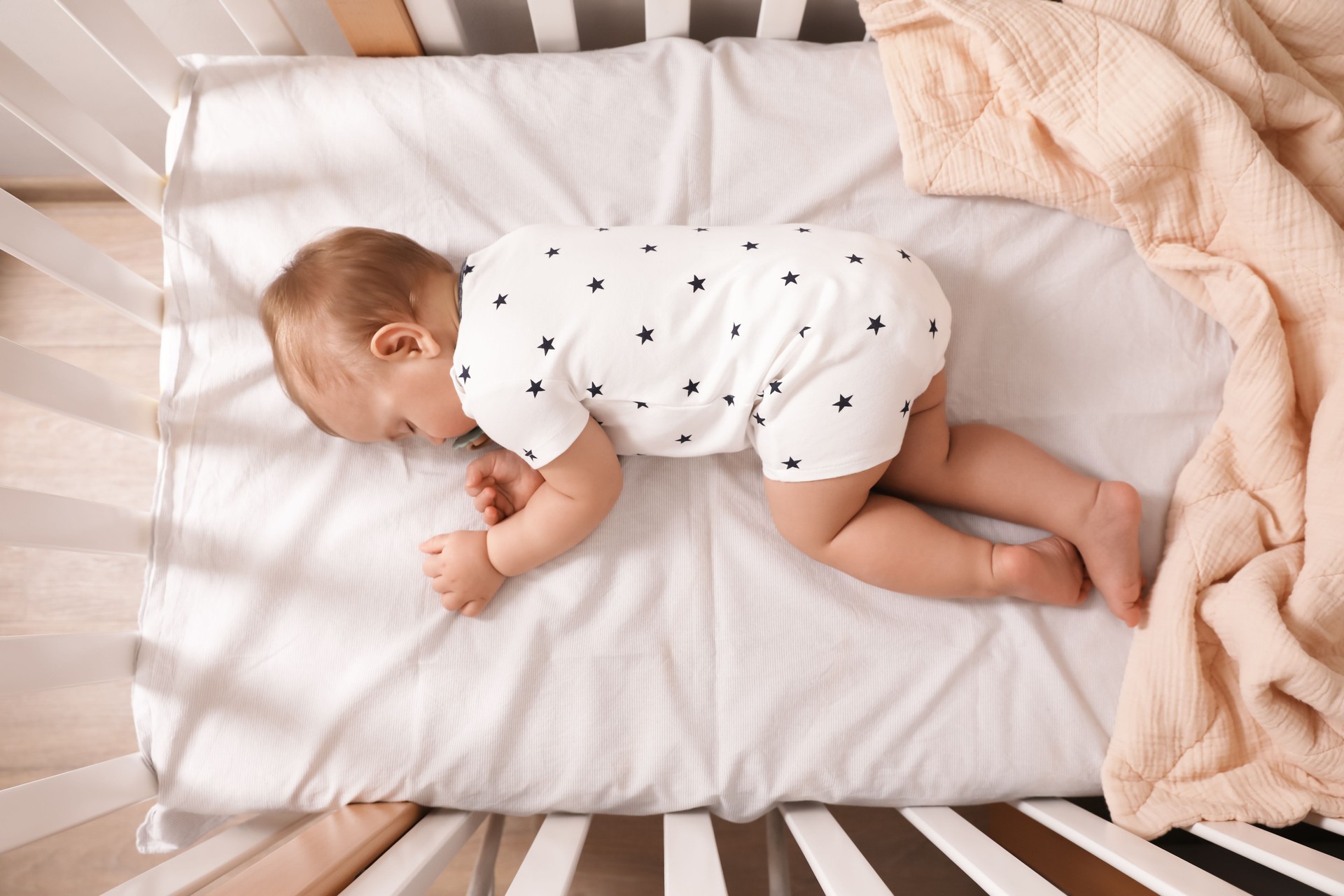 Entzückendes kleines Baby mit Schnuller, das drinnen in der Krippe schläft, Draufsicht